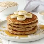 A stack of 3 ingredient oatmeal pancakes topped with banana slices and honey.