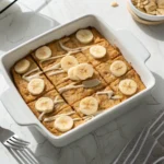 Protein baked oatmeal freshly baked in a white dish, topped with bananas and almond butter